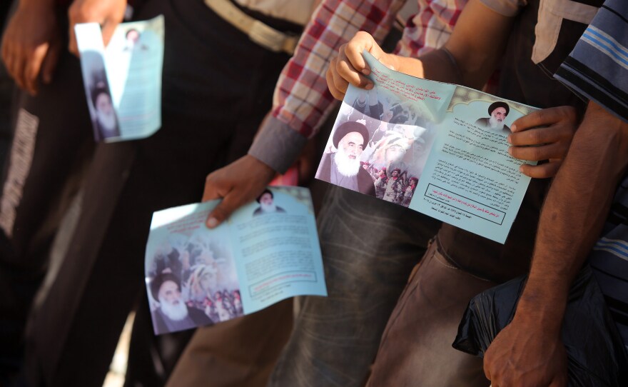 Shiite men who volunteered to join Iraq's security forces hold up pamphlets bearing images of Ayatollah al-Sistani as they queue at a recruitment center in Baghdad. The recruitment efforts of clerics in Najaf have influenced the ongoing struggle across Iraq.