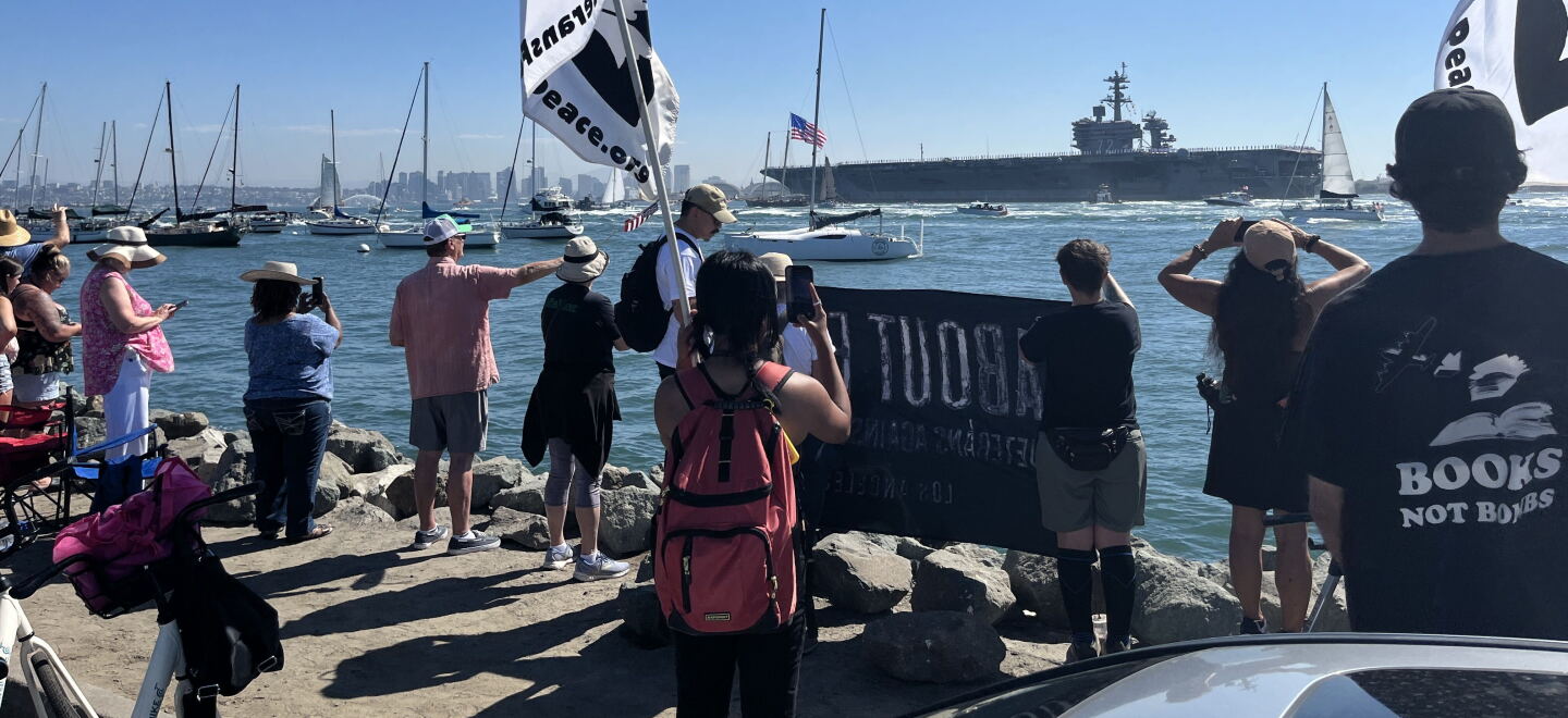 Supporters and protestors gather with signage along Shelter Island's shoreline for the USS Lincoln's arrival, Oct. 8, 2026.