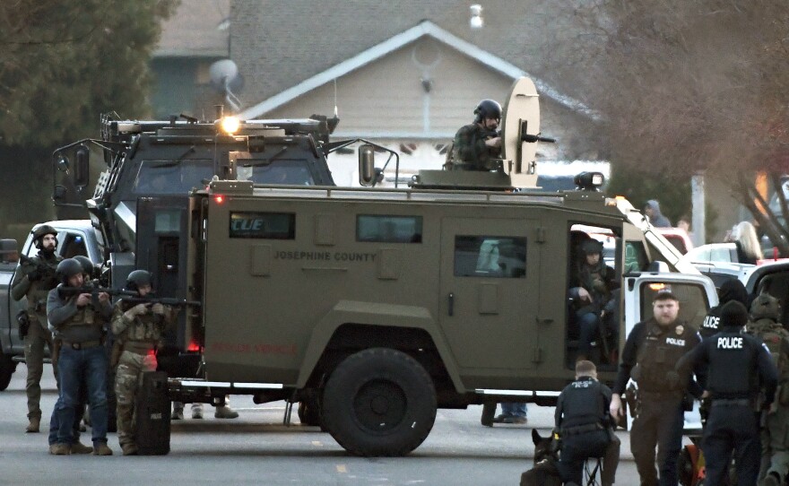 Law enforcement officers aim their weapons at a home during a standoff in Grants Pass, Ore., on Tuesday, Jan. 31, 2023. Police said the standoff involving a man suspected in a violent kidnapping in Oregon who was barricaded underneath the home had been "resolved."