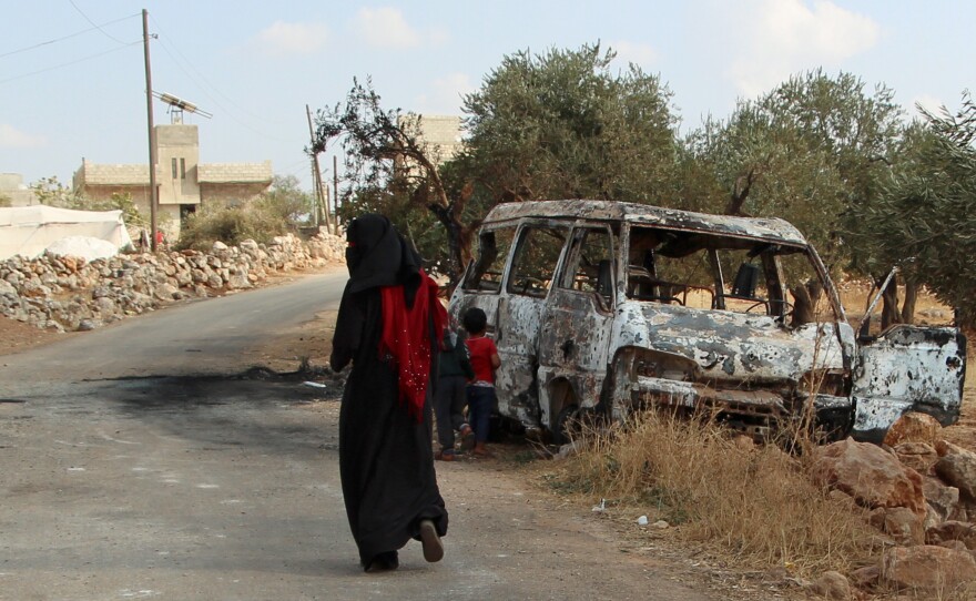 A woman walks past a wrecked van near the northwestern Syrian village of Barisha. Local residents and medical staff tell NPR that noncombatant civilians were killed and injured in the van the night of the U.S. raid on the compound of ISIS leader Abu Bakr al-Baghdadi.