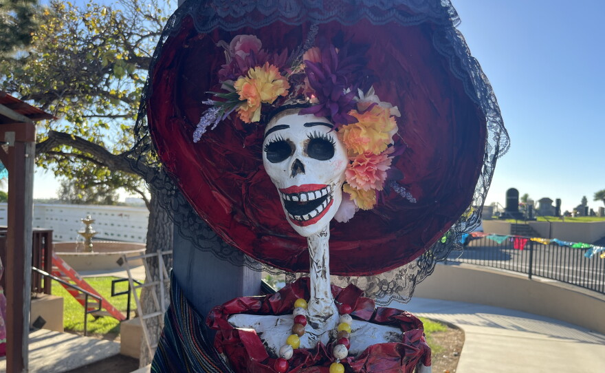 A catrina, an elegant skeleton, stands next to gravesites at La Vista Memorial Park, Oct. 26, 2026.