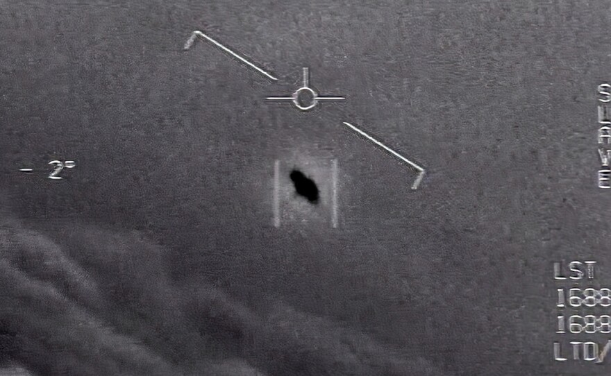 In this image from video provided by the Department of Defense, an unexplained object is seen at center as it soars high among the clouds, traveling against the wind. "There's a whole fleet of them," one naval aviator tells another, though only one indistinct object is shown.