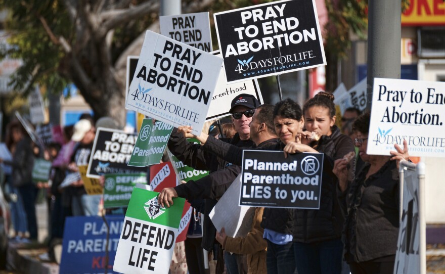 Protesters display their signs outside a Planned Parenthood health center in Los Angeles on Saturday. Together with protesters in other cities across the U.S., they gathered to demand the organization be stripped of its federal funding.