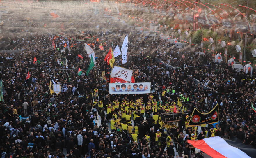 A religious procession moves through dense crowds of pilgrims in the area between the two holy shrines in Karbala, carrying flags, banners and portraits of religious figures during the Arbaeen commemoration.