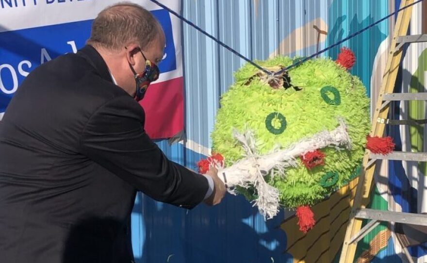 Gov. Jared Polis takes a swing at a piñata representing the COVID-19 virus, during a visit to the Adelante Community Development Clinic at Mile High Flea Market in Henderson, Colo. Feb. 26.