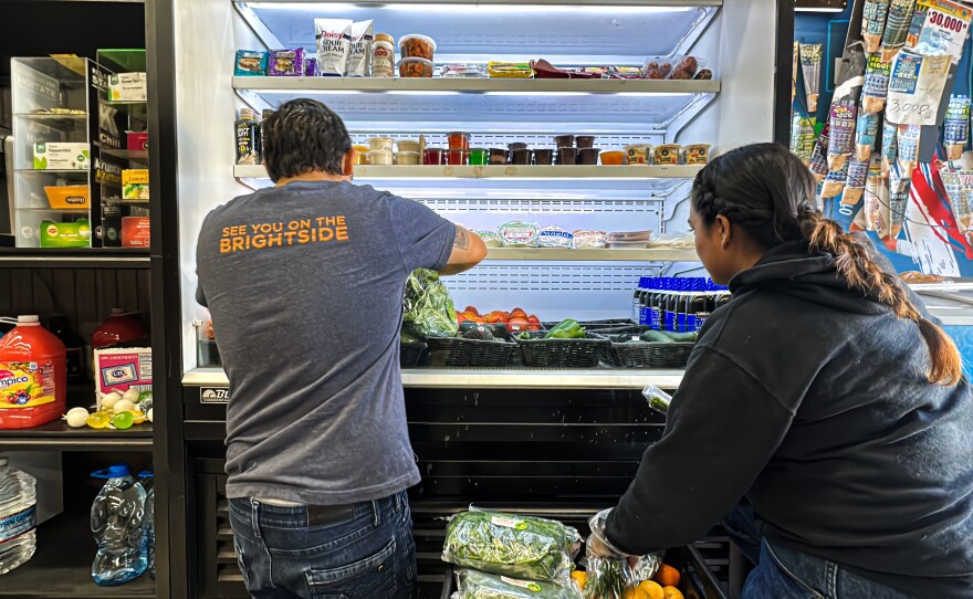 A staffer and student intern with Brightside Produce put fresh produce into a refrigerator case at Ideal Market on Nov. 21, 2023.