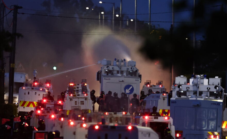 Police fire a water cannon towards rioters after they set fire to wheelie bins and removed a garden fence to use as a shield against the water cannon in Newtownabbey, Belfast, Northern Ireland, Wednesday June 10, 2026.