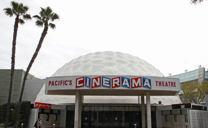 People wearing protective face masks walk by the closed Cinerama Dome theater during the coronavirus pandemic on April 18, 2020 in Los Angeles, Calif.