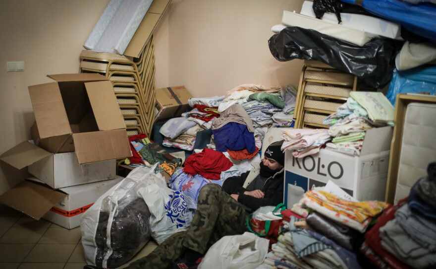 Piotr Mastalerz, exhausted from days of working around the clock as a volunteer, sleeps among piles of donated clothes and fabric.