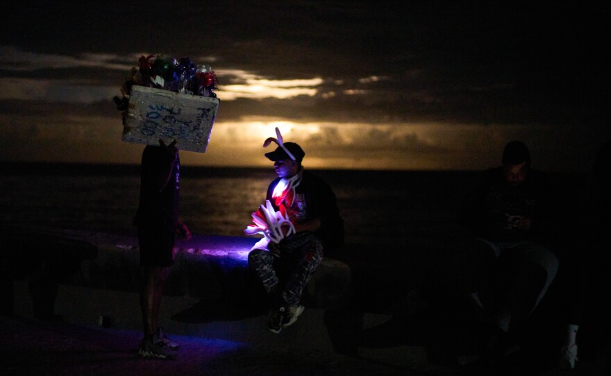 Street vendors chat on the Malecón during a blackout in Havana, Monday, March 16, 2026.