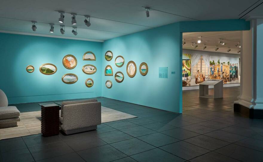 A living room-like setup overlooks small, exquisite paintings of Jamaica by Barkley L. Hendricks.