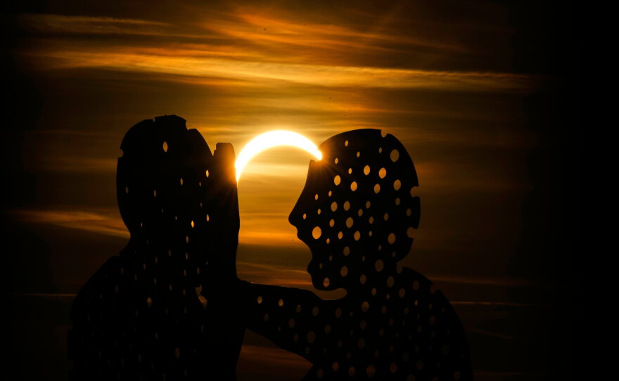 The moon partially covers the sun during solar eclipse near the Molecule Man sculpture in Berlin, Germany.