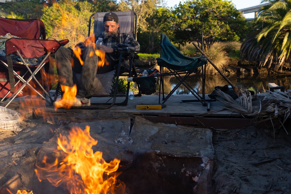 A man who goes by the name Guido sits by a camp fire on an island in the San Diego River, March 20. 2024.