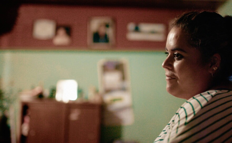 Nely Baeza, Activist, La Cantera, Guanajuato, Mexico. A Mexican woman in a striped shirt is shown in profile against a mint green wall, a slight smile on her face. The room features framed photos visible in the background. Credit: PONDEROSA PRODUCTIONS