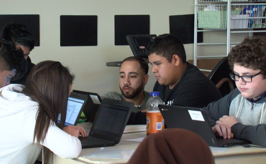 Elijah Gonzalez, center, helps a student at Thrive Public School in Rolando during English class, Dec. 5, 2016.