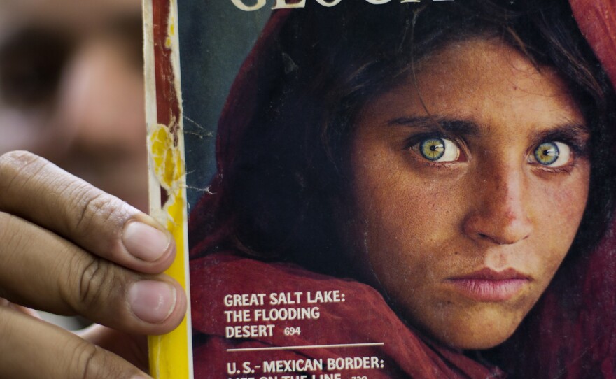 The owner of a bookstore shows a copy of <em>National Geographic</em> magazine with the photograph of Sharbat Gula, when she was around 12 years old.