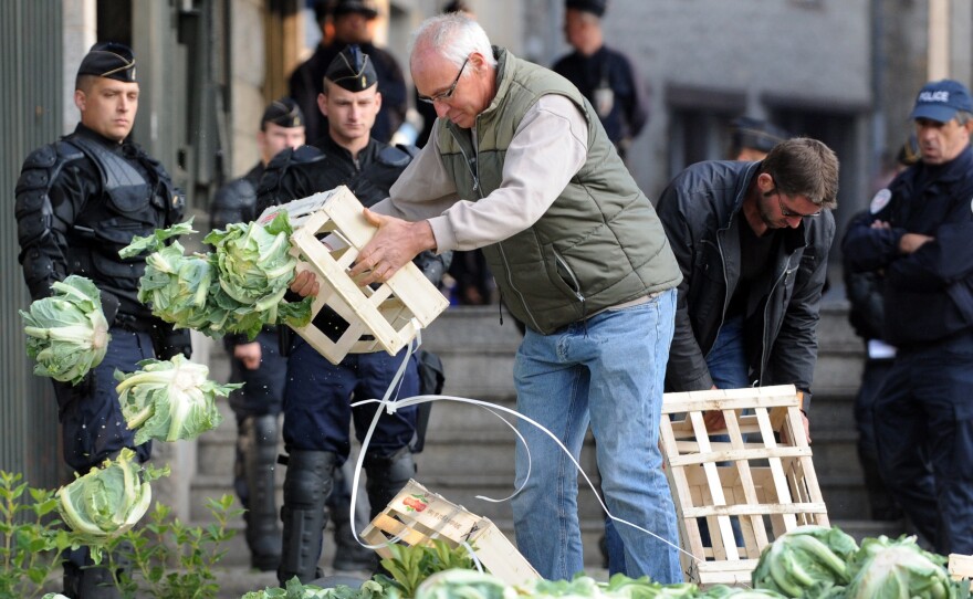 A farmer protesting falling prices dumps cauliflower in front of the prefecture building of Saint-Brieuc in northwestern France, as police look on Sept. 24.
