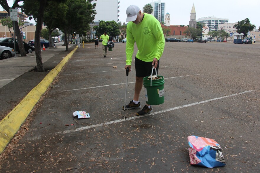 A volunteer, wearing a shirt purchased by San Diegans Together Tackling Homelessness, cleans up an Ace Parking lot downtown on July 13, 2024.
