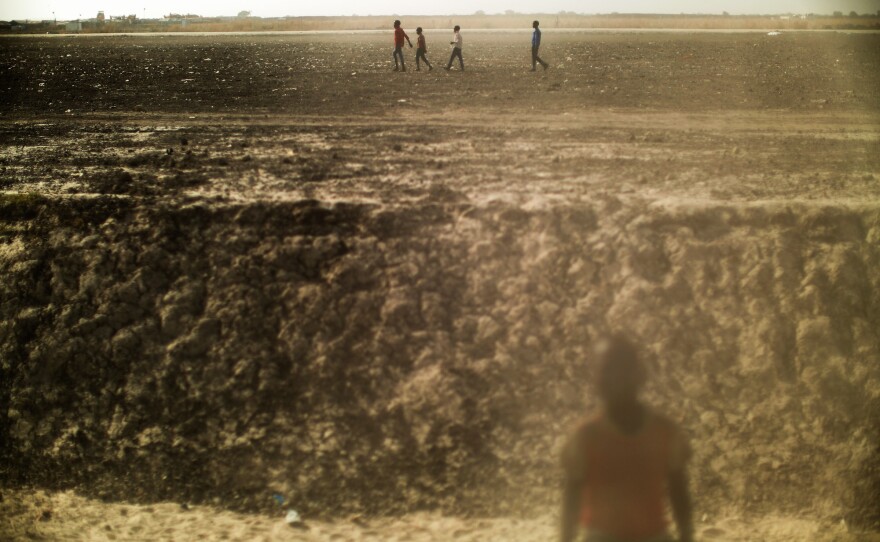 Boys walk across a dusty open plain inside the Protection of Civilians site for displaced people in Bentiu, South Sudan.