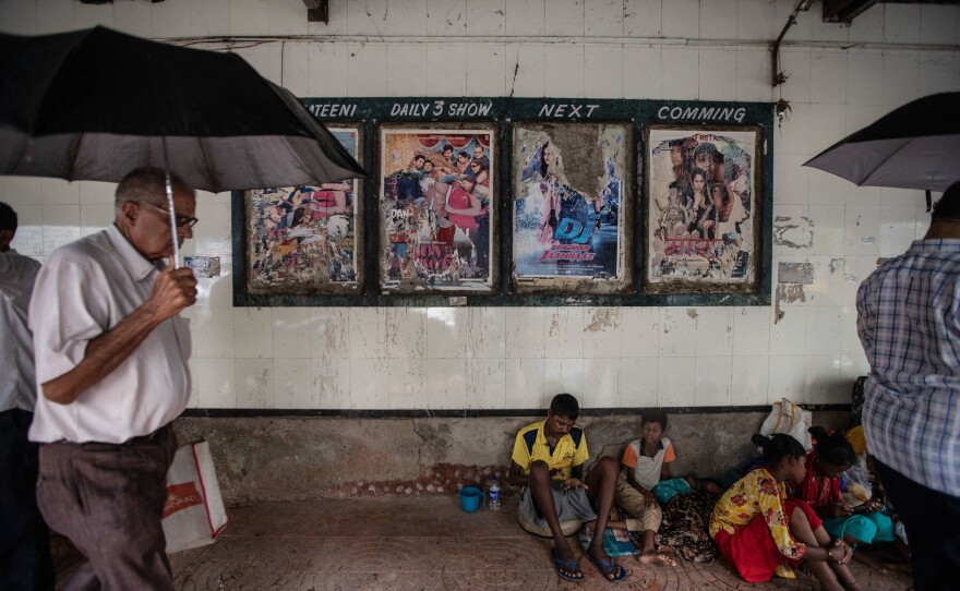 Pedestrians walk past homeless families living on the pavement outside the gates of Mumbai's Imperial Cinema.