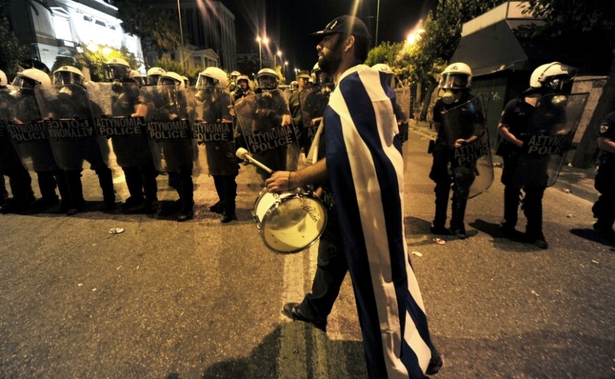A demonstrator plays drum in front of riot police outside the Greek Parliament in Athens. The protesters aren't the usual leftists and trade unionists with red banners. They're mostly middle-class Greeks waving the white and blue national flag.