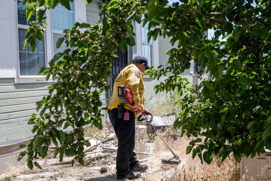 Fire captain Joseph Thompson clears the weeds for a patient in Boulevard, Calif., who is enrolled in the rural health discharge program on May 30, 2024.