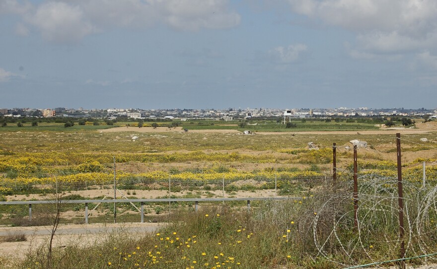 Looking into Gaza from the Israeli side of the fence, soldiers point out a white tower they say is a watch post of the militant group Hamas, and someone they say is a member of the group by a motorcycle in the olive grove at left.
