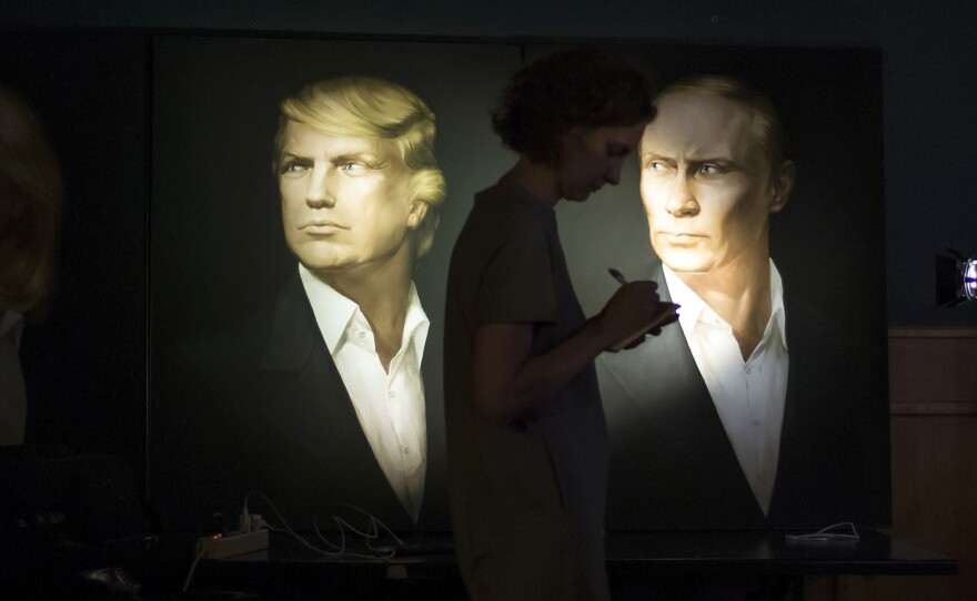 A journalist in Moscow writes notes as she watches a live telecast of the U.S. presidential election standing in front of portraits of Donald Trump and Russian President Vladimir Putin.
