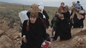 A line of Syrian refugee women, some carrying children, cross into Jordan from southern Syria. The outflow this year has been staggering. 