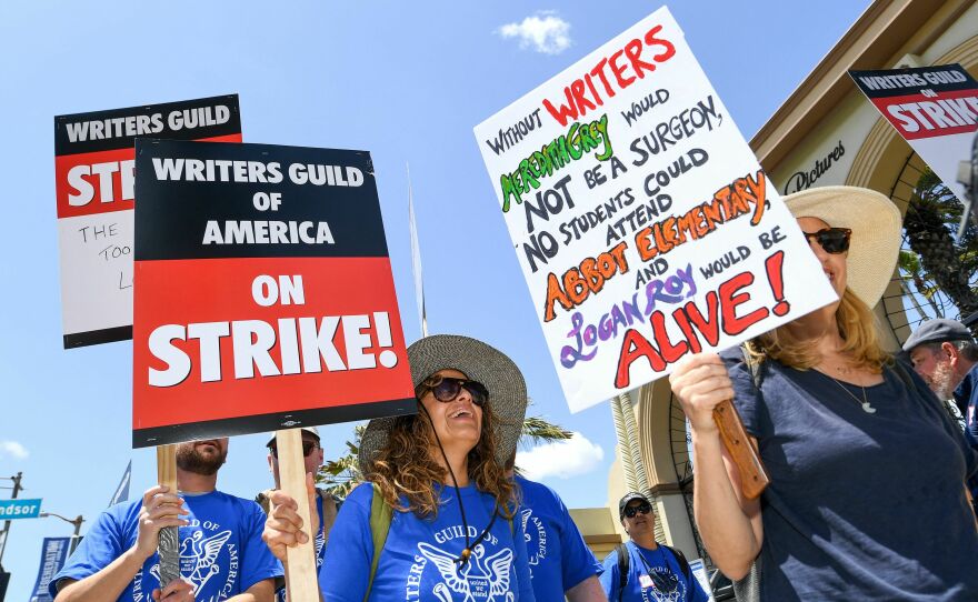 A picketer at Paramount Studios in Los Angeles carries a sign with references to the television shows <em>Grey's Anatomy, Abbott Elementary</em> and <em>Succession</em>.