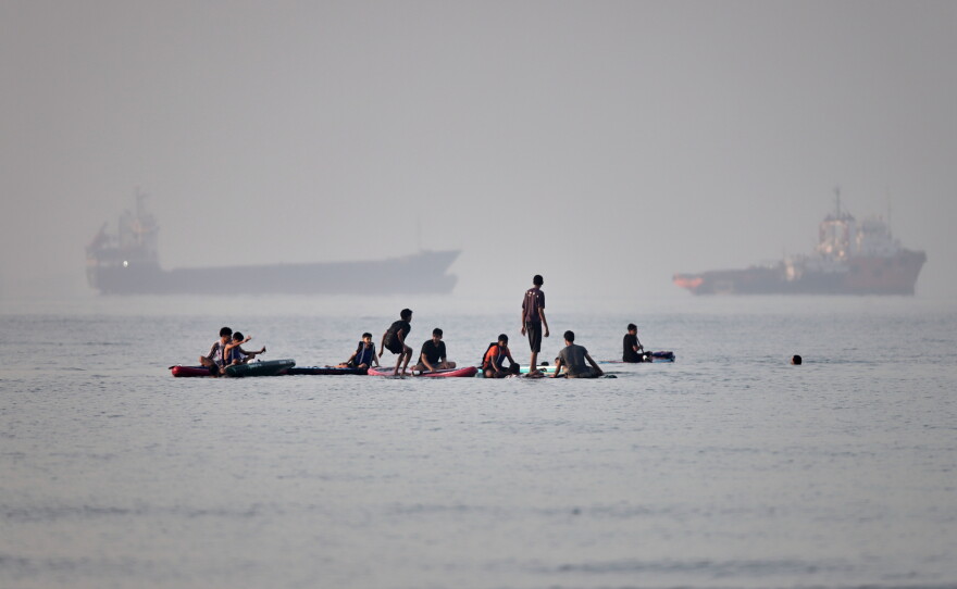 People gather on paddleboards in shallow water as cargo and service vessels are anchored in the Strait of Hormuz off Bandar Abbas, Iran, Monday, June 1, 2026.