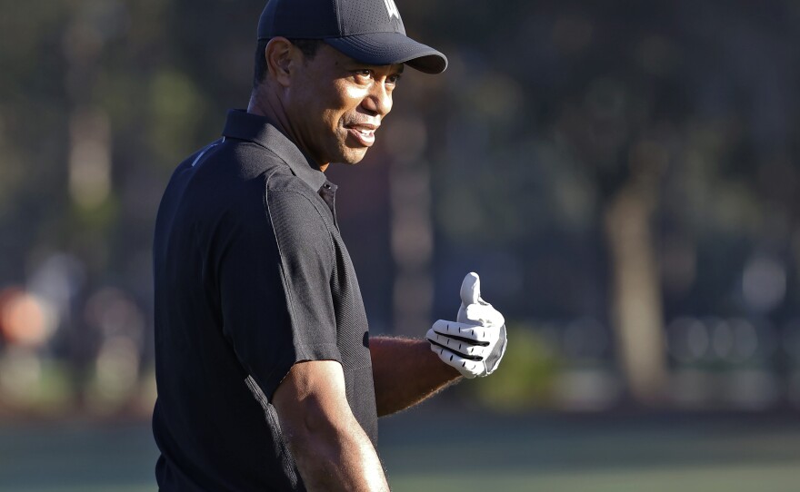 Tiger Woods smiles and gestures as he prepares to tee off during the first round of the PNC Championship golf tournament Friday in Orlando, Fla. Woods is back playing after getting injured in a car accident. He is paired with his son Charlie during the tournament.