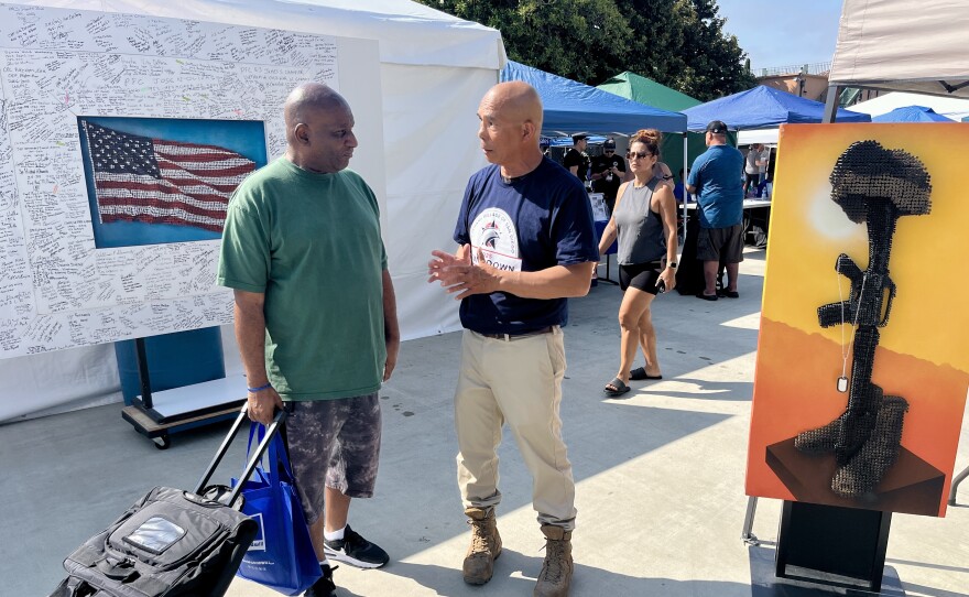 Navy veteran Joe Pisano talks about his artwork to another veteran at Stand Down 2025, Aug. 8, 2025.