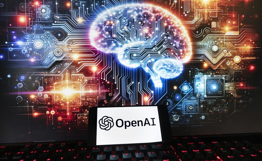 The OpenAI logo is displayed on a cellphone with an image on a computer monitor generated by ChatGPT's Dall-E text-to-image model in Boston on Dec. 8, 2023.