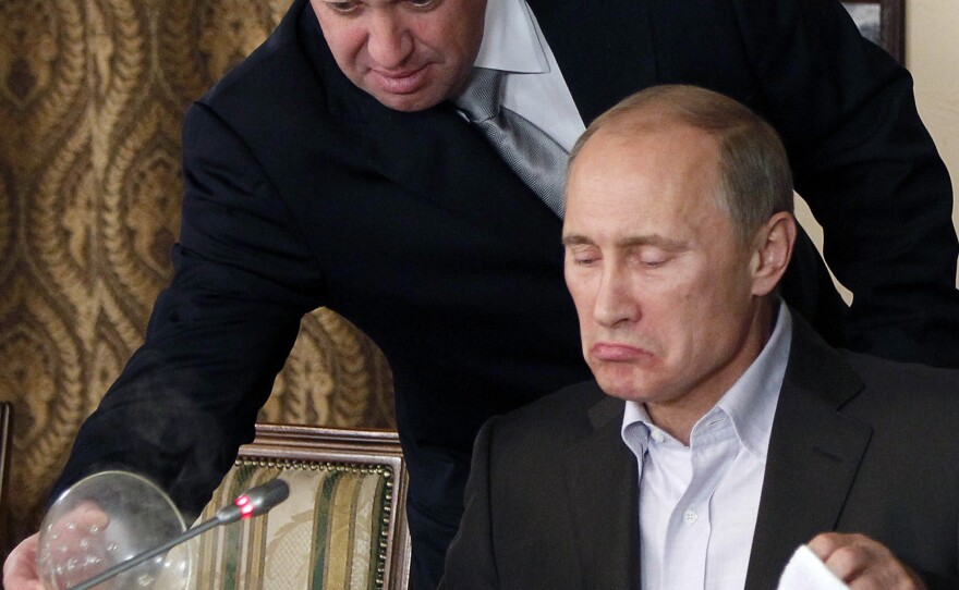 In this Nov. 11, 2011, file photo, Yevgeny Prigozhin, left, serves food to then-Russian Prime Minister Vladimir Putin during dinner at Prigozhin's restaurant outside Moscow, Russia. Friday, Prigozhin, along with 12 other Russians and three Russian organizations, was charged by the U.S. government as part of a vast and wide-ranging effort to attack the 2016 U.S. presidential election.