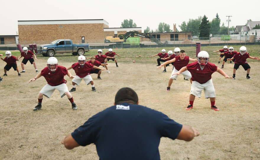 Alexander High School teacher and football team defensive coordinator Mike Rizzo, center, leads the high school and junior high teams through warm up stretches at a practice in August. Most of the players on the team, which plays in a six-man division, have never played organized football before.