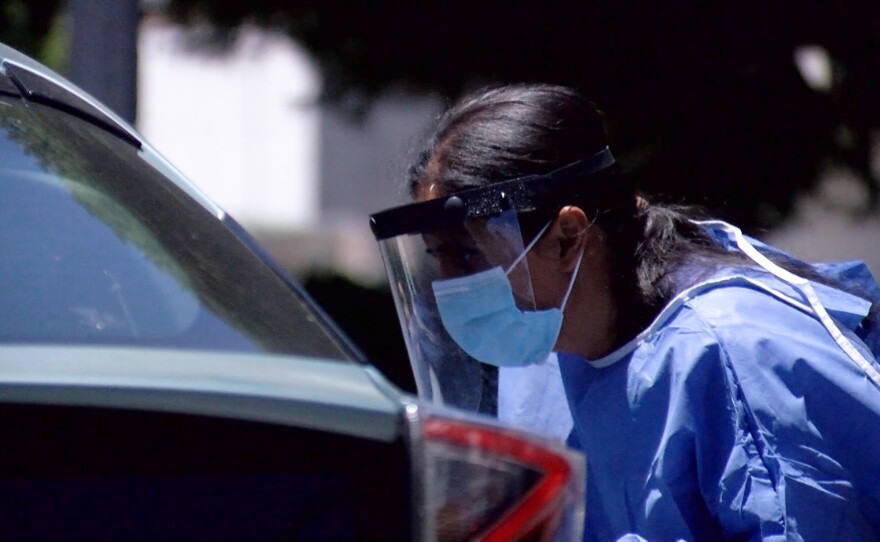 A a county employee waits for a person to swab themselves for a COVID-19 test in a University of San Diego parking lot, July 15, 2020.