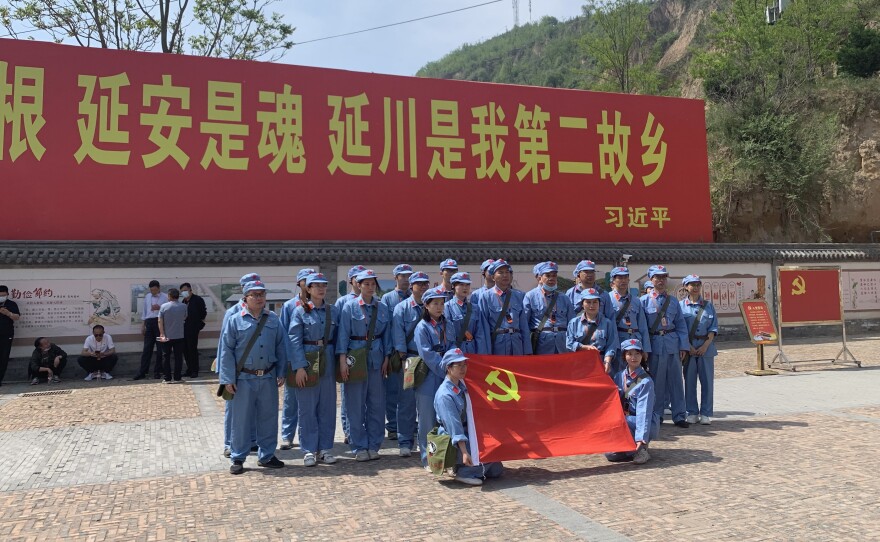 Tourists dressed up as People's Liberation Army soldiers pose in Liangjiahe village, where a teenage Xi Jinping spent seven years doing hard labor. Today the village is a popular red tourism site. The sign displays a quote from Xi: "Liangjiahe is where my roots are, and my soul. It is my second home."