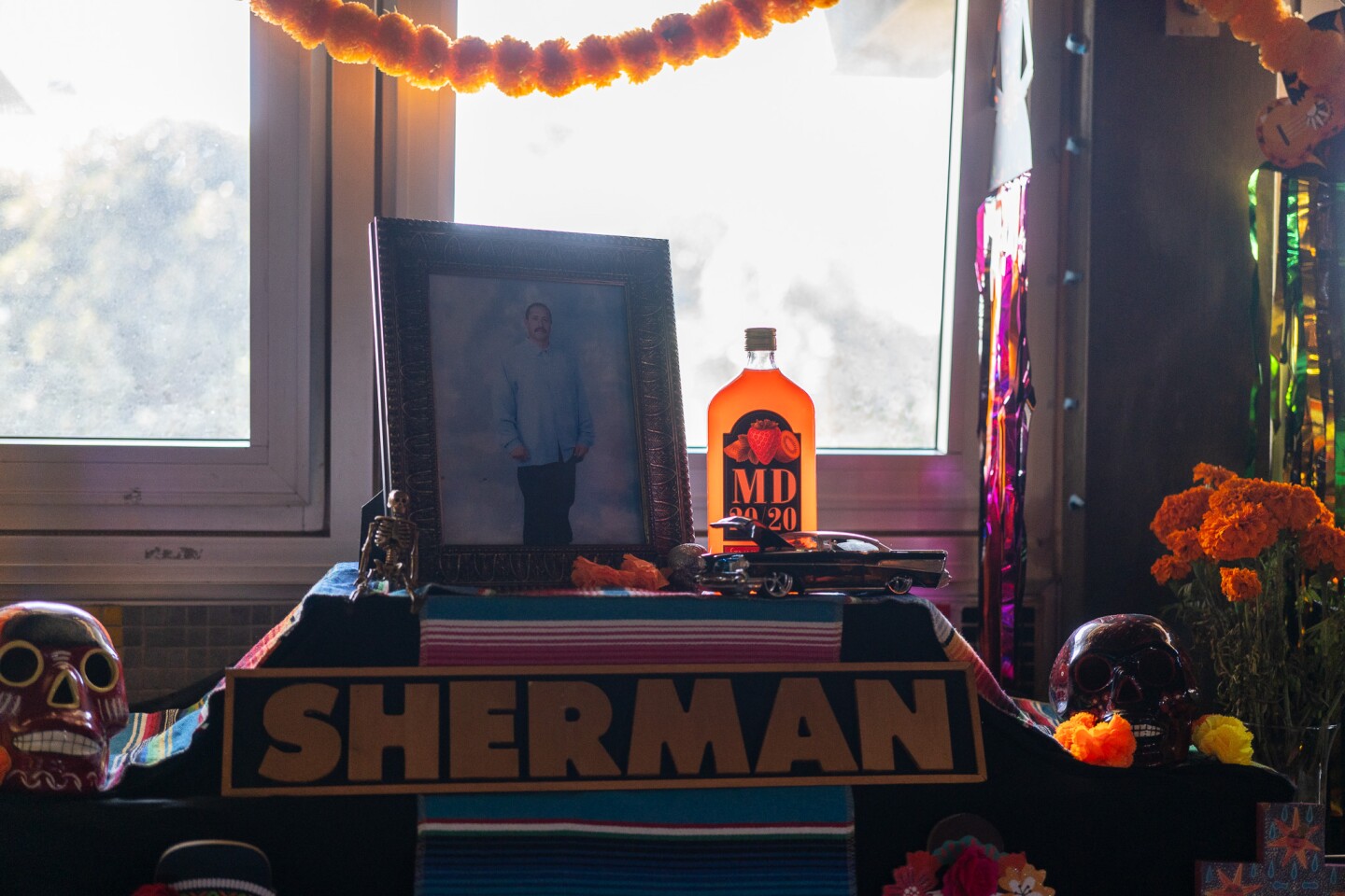 A photo of a lost loved one alongside a bottle of strawberry-kiwi MD 20/20 and a model low-rider car are prominently featured on an altar at the Sherman Heights Community Center in San Diego on Oct. 17, 2023.