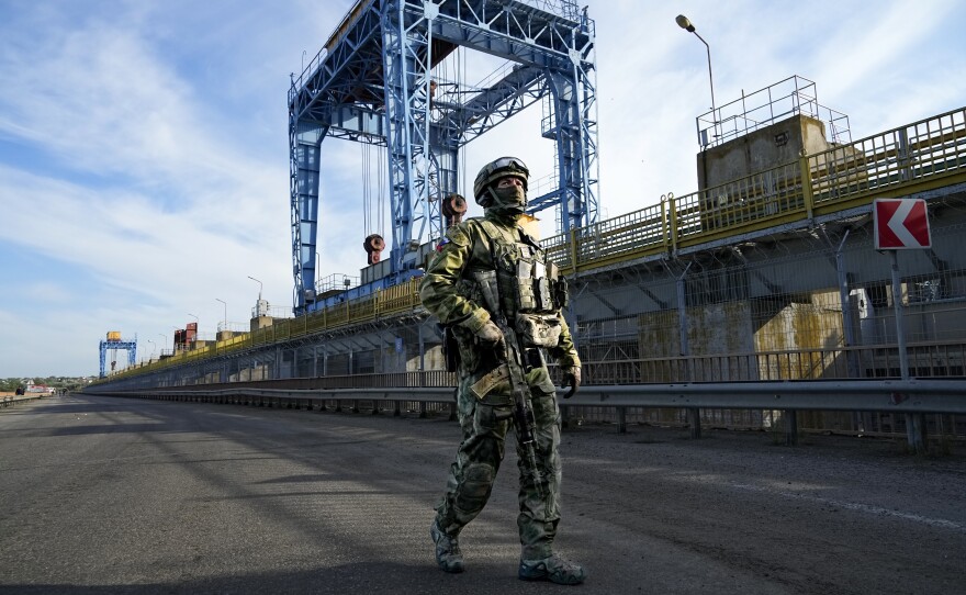 A Russian soldier patrols an area at the Kakhovka Hydroelectric Station on May 20, 2022, in a photograph taken during a trip organized by the Russian Ministry of Defense. The blue gantry cranes, which control locks along the dam, can be seen in the background.