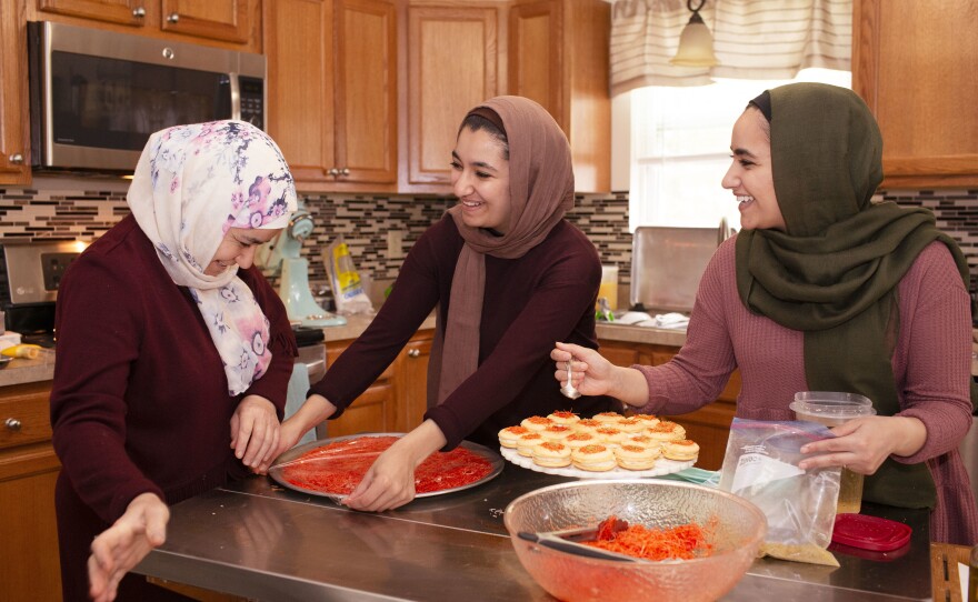 From left, Huda Attar and her daughters, Eslah and Shorook, in the kitchen baking. Huda is teaching Eslah how to make <em>knafeh</em>, a Middle Eastern dessert consisting of a thin noodle pastry stuffed with cheese, soaked in syrup and topped with pistachios.