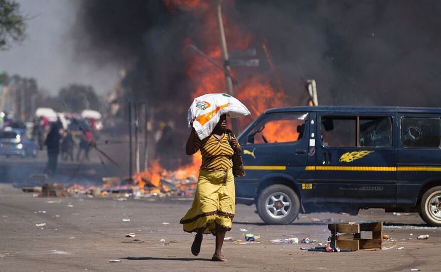 A woman carrying groceries on her head runs away as Zimbabwe's opposition supporters set up a burning barricade.