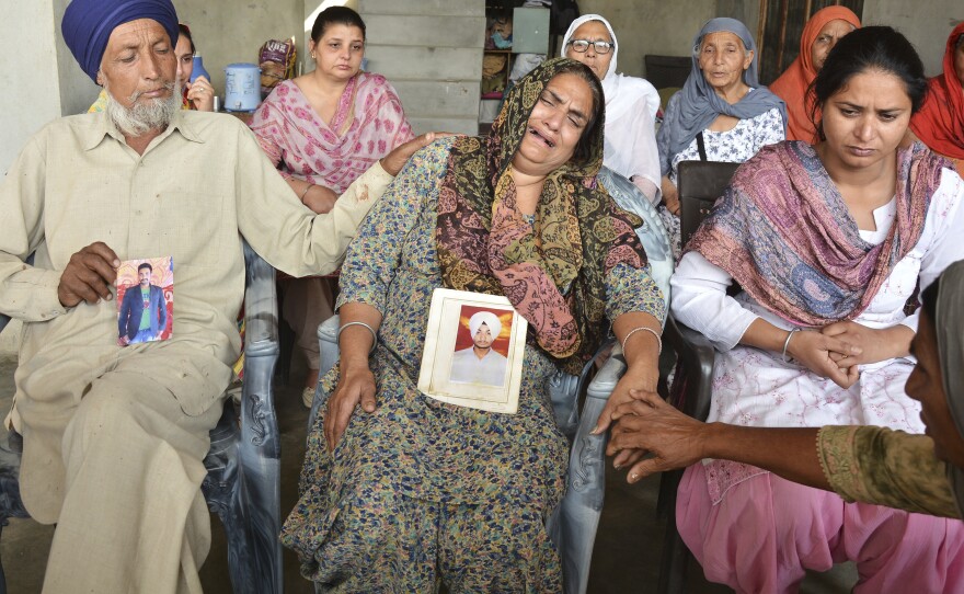Hardeep Sing (left) and Sushwinder Kaur (center) mourn holding portraits of their son Manjinder Singh, one of the 39 Indian workers whose bodies were found buried northwest of Mosul.