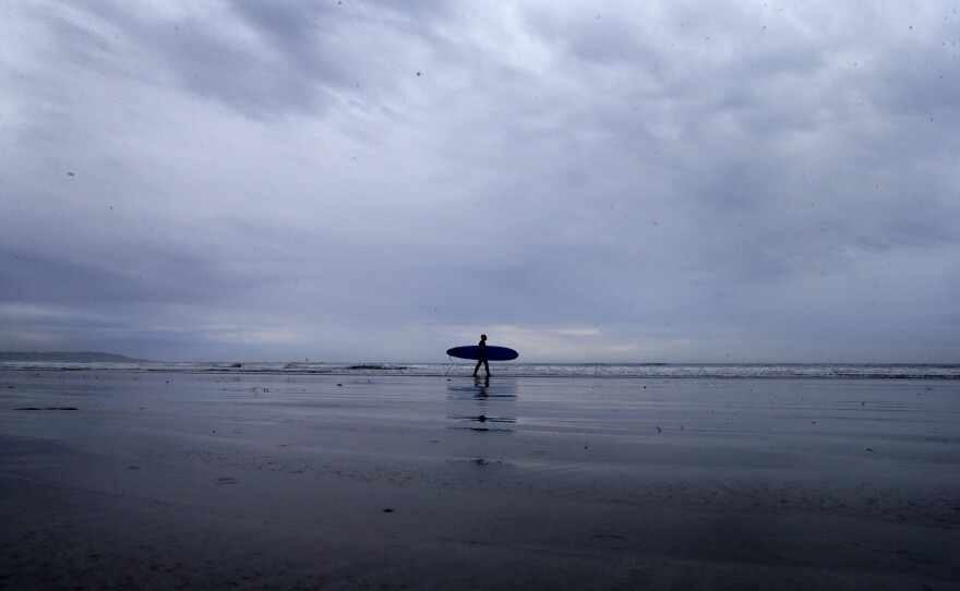A lone surfer makes his way into the water as storm clouds come ashore in San Diego, Dec. 2, 2014.