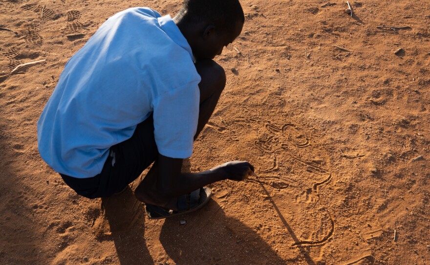 Paris has taught himself to draw. Above, he sketches in the sand at school.