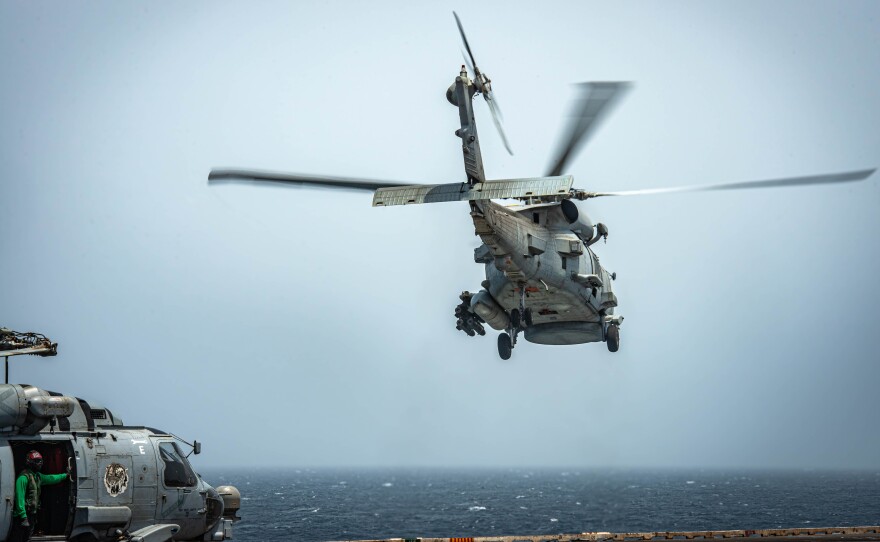 A gray Navy helicopter takes off from the flight deck of the USS Nimitz while deployed as another helicopter sits on the deck.