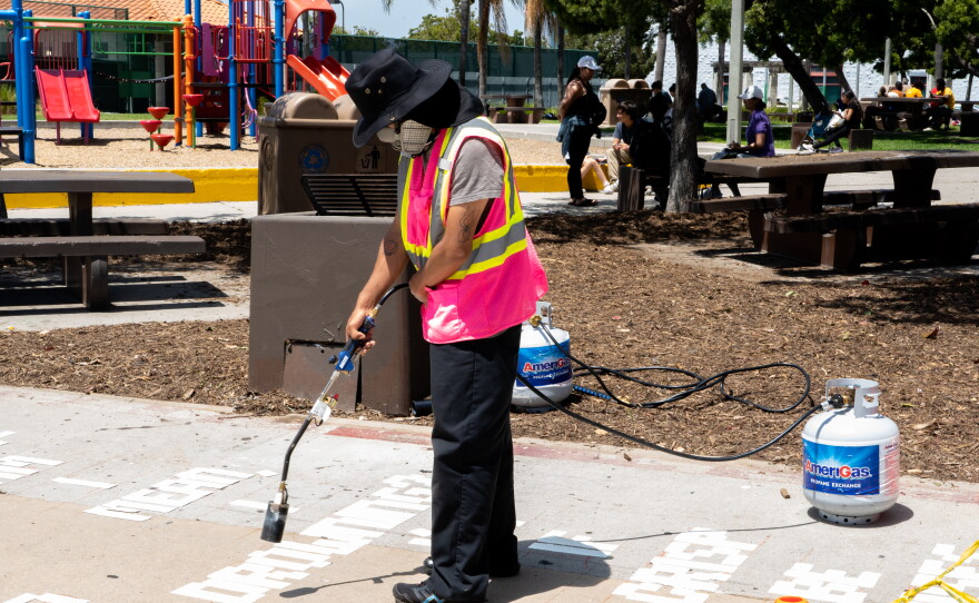 A project worker burns the letters of poetry onto the pavement of a City Heights alley on Tuesday, June 18, 2024.