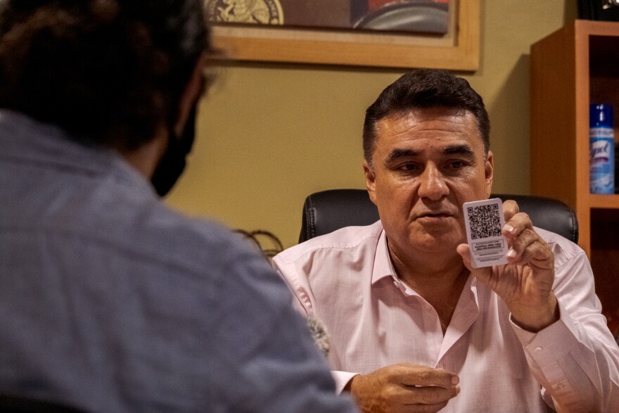 Jesus Alejandro Ruiz Uribe, the federal delegate that oversees Baja California's social programs, is shown here at the offices of the Secretaria de Bienestar in Tijuana, Mexico. Nov. 03, 2021. He holds up his card to show the QR code that connects scanners with a database for COVID-19 vaccination proof.