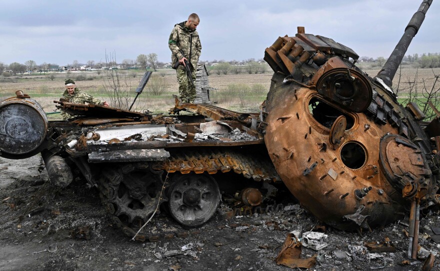 Ukrainian servicemen look at a destroyed Russian tank on a road in the village of Rusaniv, in the Kyiv region on April 16, 2022.