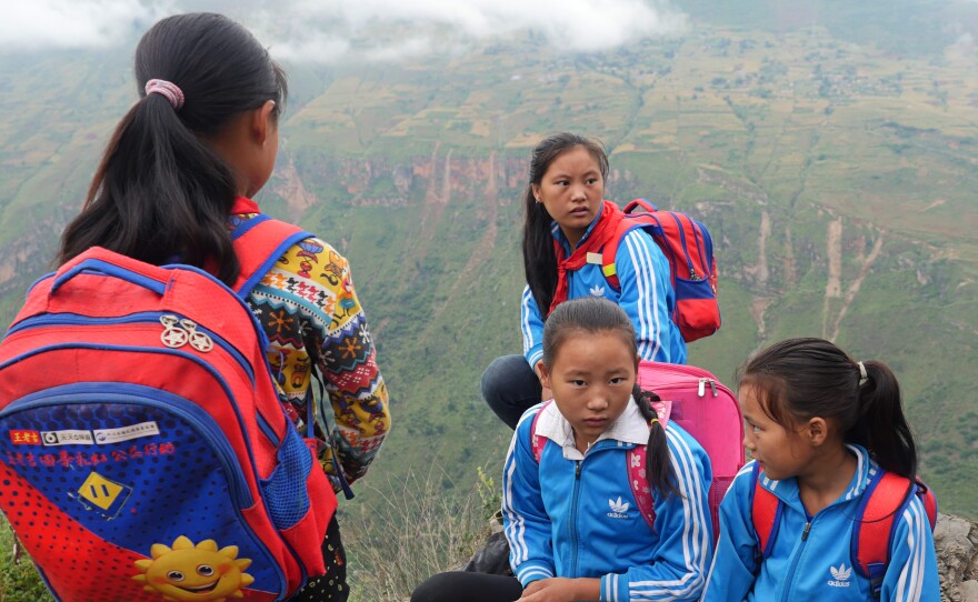Ethnic Yi schoolgirls take a break halfway down the mountain, on their way from their homes in Atule'er village to their first day of school in a new semester. The difficulty of getting up and down the mountain has made it hard for villagers to shake off poverty, and made it challenging for their children to attend school.